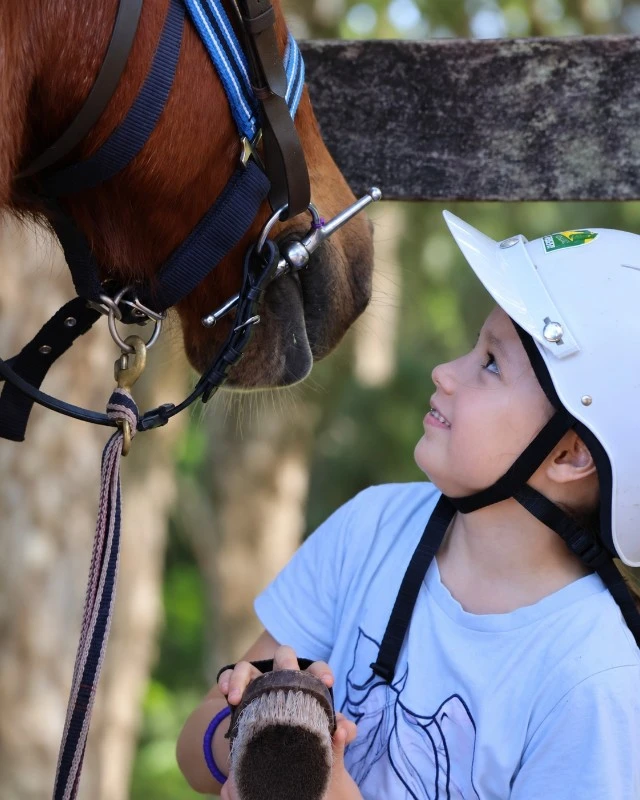 Child wearing a helmet gazes up at a horse nose-to-face contact during a supervised ride.