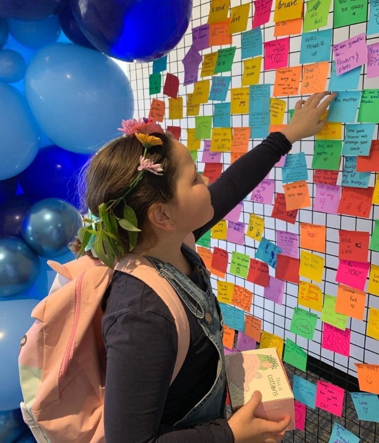 A girl adding a colourful Post-it note to the Beautiful Minds® Love Bomb Wall