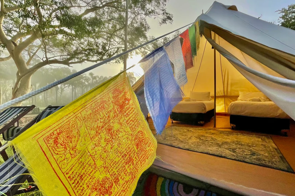 Bell tent surrounded by trees with colourful fabric and a welcoming interior